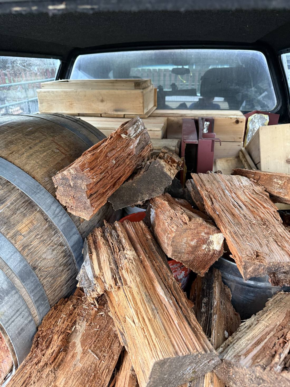 A truck bed loaded with split firewood and a wine barrel